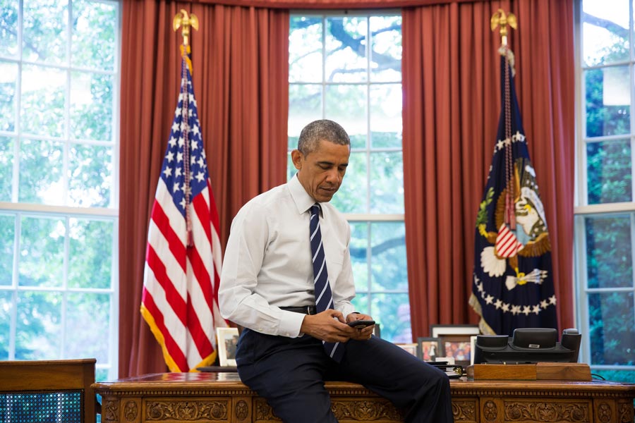 Barack Obama looking at a phone in the Oval Office